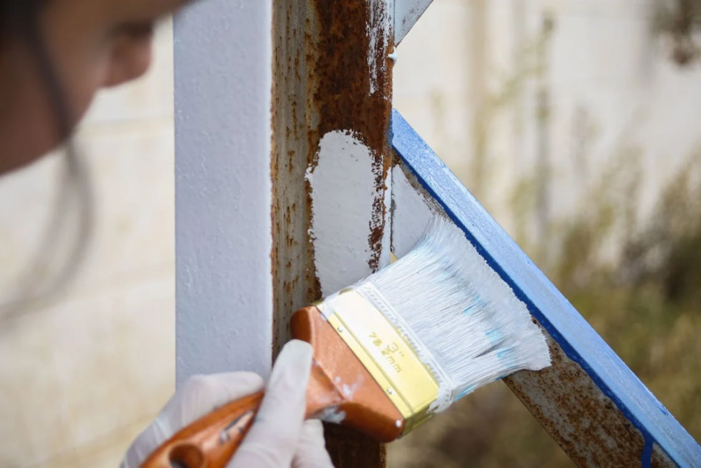 Applying a protective coating to a metal railing with a paintbrush.